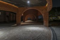 the lights are on in an empty tunnel area at night time, illuminated with streetlights and brick arches