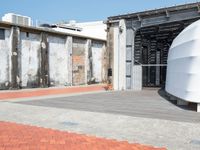 a red brick sidewalk next to concrete buildings and a large metal wall that has been boarded