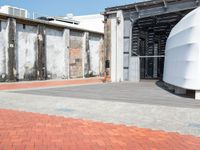 a red brick sidewalk next to concrete buildings and a large metal wall that has been boarded