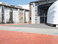 a red brick sidewalk next to concrete buildings and a large metal wall that has been boarded