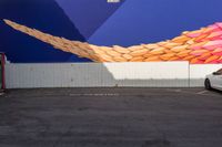 a white car parked in a parking lot in front of a colorful wall that has some lines painted on it