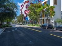 a street with parked cars on the side of it and a large mural on the side of building