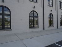 a small fire hydrant on a cement walkway in front of brick building with arched windows