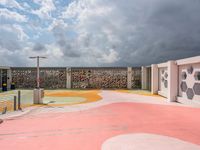 a pink basketball court and a concrete wall with white designs against a cloudy background with a street light