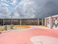 a pink basketball court and a concrete wall with white designs against a cloudy background with a street light