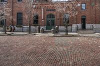 two parking meters are in front of an old brick building with large windows, and some trees and other bushes and bushes