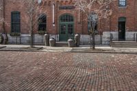 two parking meters are in front of an old brick building with large windows, and some trees and other bushes and bushes