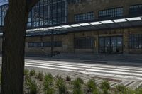 an old building with many windows and bushes near it and the road outside is not paved