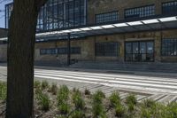 an old building with many windows and bushes near it and the road outside is not paved