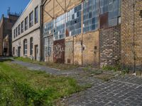 an old brick building sitting next to a sidewalk and field of grass with buildings in the background