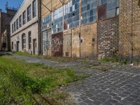 an old brick building sitting next to a sidewalk and field of grass with buildings in the background