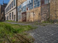 an old brick building sitting next to a sidewalk and field of grass with buildings in the background