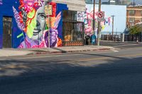 two people walk down the street in front of a building with various colorful street art