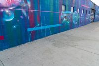 the colorful painted graffiti is on the side of a building near a blue fire hydrant