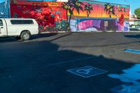 the parking lot features a mural with palm trees on it and there is a white van parked near the parked cars