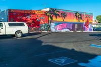 the parking lot features a mural with palm trees on it and there is a white van parked near the parked cars