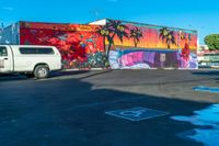 the parking lot features a mural with palm trees on it and there is a white van parked near the parked cars