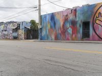 a multicolored building on a side walk with graffiti on the outside and one painted by a man in the middle