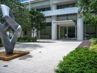 a modern abstract stainless statue sitting in front of an office building on the edge of a walkway