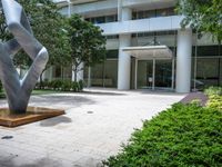 a modern abstract stainless statue sitting in front of an office building on the edge of a walkway