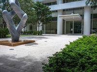 a modern abstract stainless statue sitting in front of an office building on the edge of a walkway