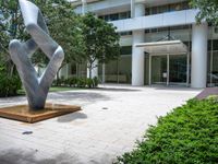 a modern abstract stainless statue sitting in front of an office building on the edge of a walkway