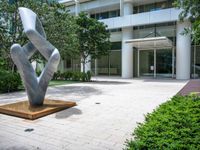 a modern abstract stainless statue sitting in front of an office building on the edge of a walkway