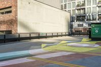 a woman sitting on the sidewalk on a skateboard painting in the street, a large building with windows behind it