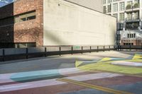 a woman sitting on the sidewalk on a skateboard painting in the street, a large building with windows behind it