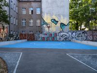 a basketball court in front of an apartment building with graffiti on it's wall