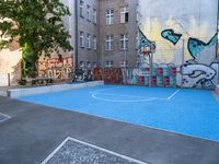 a small outdoor basketball court with street art in a building yard area with graffiti painted on the wall