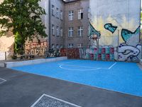 a small outdoor basketball court with street art in a building yard area with graffiti painted on the wall