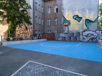 a small outdoor basketball court with street art in a building yard area with graffiti painted on the wall