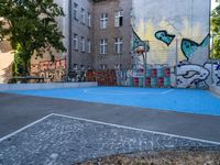 a small outdoor basketball court with street art in a building yard area with graffiti painted on the wall