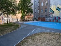 an outside basketball court that is painted blue in front of a building with graffiti on it