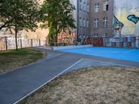 an outside basketball court that is painted blue in front of a building with graffiti on it