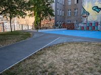 an outside basketball court that is painted blue in front of a building with graffiti on it