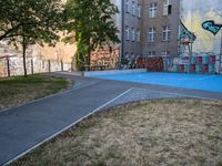 an outside basketball court that is painted blue in front of a building with graffiti on it