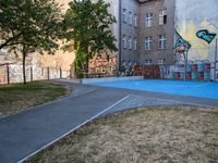 an outside basketball court that is painted blue in front of a building with graffiti on it