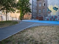 an outside basketball court that is painted blue in front of a building with graffiti on it