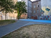 an outside basketball court that is painted blue in front of a building with graffiti on it