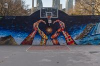 the basketball court has a mural depicting two hands reaching for a heart shaped item with buildings in the background