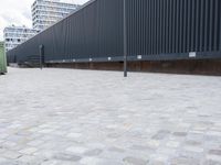a white and black dog runs near the fence on an outdoor area with a building in the background