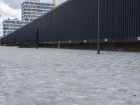 a white and black dog runs near the fence on an outdoor area with a building in the background