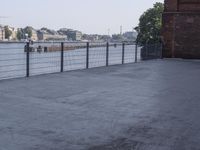 the street is paved with concrete, surrounded by water and buildings, and a chain link fence