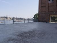 the street is paved with concrete, surrounded by water and buildings, and a chain link fence