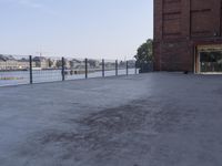 the street is paved with concrete, surrounded by water and buildings, and a chain link fence