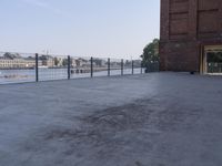 the street is paved with concrete, surrounded by water and buildings, and a chain link fence