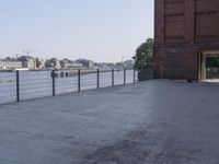 the street is paved with concrete, surrounded by water and buildings, and a chain link fence