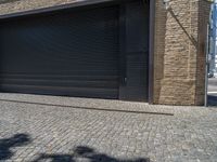 two windows in the side of a brick building, with a black garage door and brown door